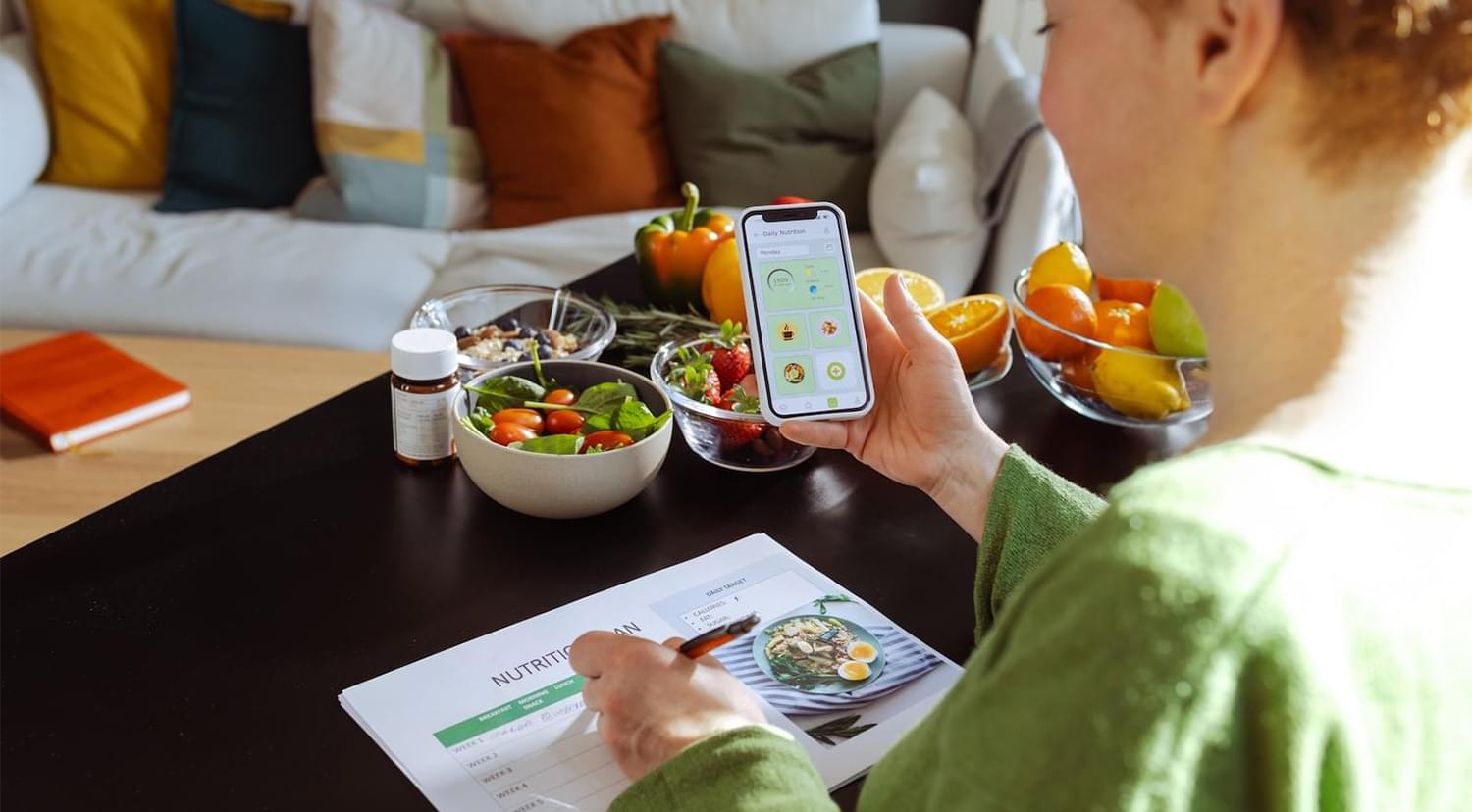 A mid adult woman checking the nutrition facts and calories intake of the meals on her smart phone. She is holding a nutrition plan